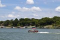 Pontoon boat motoring out past houses and boat docks on the shore on a sunny day at the lake