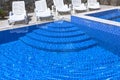 Pool with blue water ladder for descent and ascent into the water. The sun loungers are empty by the pool