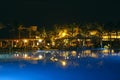 Pool and evening hotel on vacation. People relax by evening near pool. Lights of evening hotel are reflected in pool water in Royalty Free Stock Photo