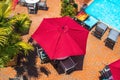 Poolside textured red umbrellas over tables and chairs beside lounges covered in beach towels and potted palms on orange tile deck Royalty Free Stock Photo