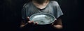 a poor child holding a empty plate. dark background. Poverty. Help needed.