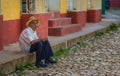 Poor Cuban senior man in traditional colorful alley with colonial house, in old town, Cuba, America.