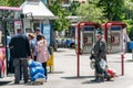 Poor and dirty homeless man standing on the street watch other people entering the city bus.