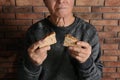 Poor elderly man with bread near brick wall