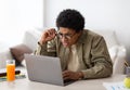 Poor eyesight. Black teenager in glasses squinting his eyes while using laptop computer for online education at home Royalty Free Stock Photo