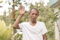 A poor but friendly old asian man waves his hand. A simple villager wearing a white shirt