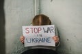 Poor girl protesting war conflict raises banner with inscription Stop war in Ukraine. Kid sits near old broken wall and calls No