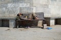 Poor homeless beggar man or refugee sleeping on a dirty wooden bench in a one-way street in the city during day time. Social