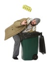 Poor homeless man digging in trash bin on white