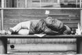 Poor homeless man or refugee sleeping on the wooden bench on the urban street in the city, social documentary concept, black and w Royalty Free Stock Photo