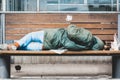 Poor homeless man or refugee sleeping on the wooden bench on the urban street in the city, social documentary concept Royalty Free Stock Photo