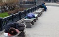 Poor homeless man or refugee sleeping on the wooden bench on the urban street in the city, social documentary concept