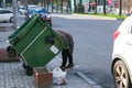 Poor hungry woman looking for food in a trash can on the street. The homeless person has no Royalty Free Stock Photo