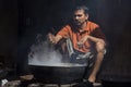 Poor man cooks in old wok the fire, India