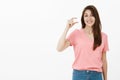Poor me just little. Portrait of attractive european brunette in pink t-shirt, shaping small or tiny object and smiling