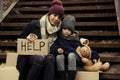 Poor mother and daughter with HELP sign sitting on stairs