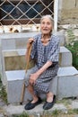 Poor old Bulgarian woman with walking cane and worn out, shabby dress sitting on stairs on the street of Varna Royalty Free Stock Photo