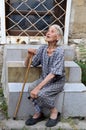 Poor old Bulgarian woman with walking cane and worn out, shabby dress sitting on stairs on the street of Varna Royalty Free Stock Photo