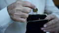 Poor pensioner putting coin in wallet with trembling hands, financial crisis