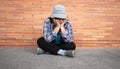 Poor tired stressed depressed elderly Asian woman homeless sitting on the street in the shadow of the building and begging for