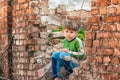 Poor and unhappy orphan boy, sitting on the ruins and ruins of a destroyed building. Staged photo Royalty Free Stock Photo
