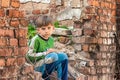 Poor and unhappy orphan boy, sitting on the ruins and ruins of a destroyed building. Staged photo