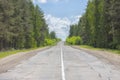 A poorly-paved rural two-lane road, deciduous forest, cloudy sky, highway to the horizon Royalty Free Stock Photo