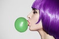 Pop art woman portrait wearing purple wig. Blow a green bubble