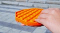 Kid hands close-up, playing with orange silicone antistress fidget toy outdoors