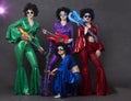 A pop music group sings in a nightclub. Young girls dressed in retro seventies costumes