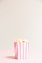 Popcorn bag with white and pink stripes at the light neutral backdrop. Empty minimalistic background. Romantic movie