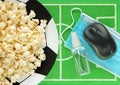 Popcorn on big plate like soccer ball, computer mouse, sanitizer with blue medical mask placed on green felt mini football field. Royalty Free Stock Photo