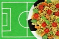 Tricolor pasta in form of football symbols, basil, red cherry tomato on plate like soccer ball, dish mat like football field. Royalty Free Stock Photo