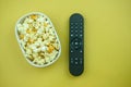 Popcorn bowl and remote control on yellow background Royalty Free Stock Photo