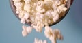 Popcorn falling from bowl on blue background, perfect snack for watching movie at home.