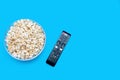Popcorn in a glass bowl and a TV remote control on a blue background Royalty Free Stock Photo