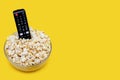 Popcorn in a glass bowl and a TV remote control on a yellow background Royalty Free Stock Photo