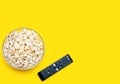 Popcorn in a glass bowl and a TV remote control on a yellow background Royalty Free Stock Photo