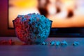 Popcorn in a glass plate on the background of the TV. Color bright lighting, blue and red. Background Royalty Free Stock Photo