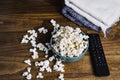 Popcorn, remote control and blanket on wooden table