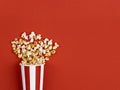 Popcorn spilled from a white and red striped bucket on a bright red background. Royalty Free Stock Photo