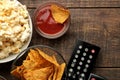 Popcorn and various snacks, TV remote on a brown wooden background. concept of watching movies at home. view from above Royalty Free Stock Photo
