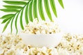 Popcorn in a white bowl on a background of palm leaves, on a white plate. Selective focus. Corn snacks. close-up Royalty Free Stock Photo