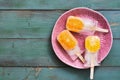 Popsicle.Fruity ice cream with orange slices on a pink plate, green wooden background. Summer dessert. top view, copy space.