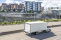 Popular day cab big rig semi truck transporting commercial cargo in long box trailer driving on the divided highway road in urban