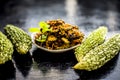 Popular dish for serving in lunch i.e. Bitter gourd with spices and vegetables on wooden surface in a glass plate with raw karela,