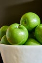 Green Granny Smith apples in a white bowl and dark brown background.