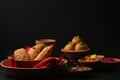 Popular Indian Sweet Besan Laddoo gram flour sweet balls and Gujia or Karanji arepopular Holi snacks served in earthen bowls.