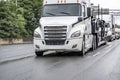 Popular industrial car hauler big rig white semi truck transporting cars on semi trailer driving on the wet highway road in front