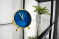 Popular round clock with hour and minute hands on glossy surface in office. Small golden tabletop clock with blue analog